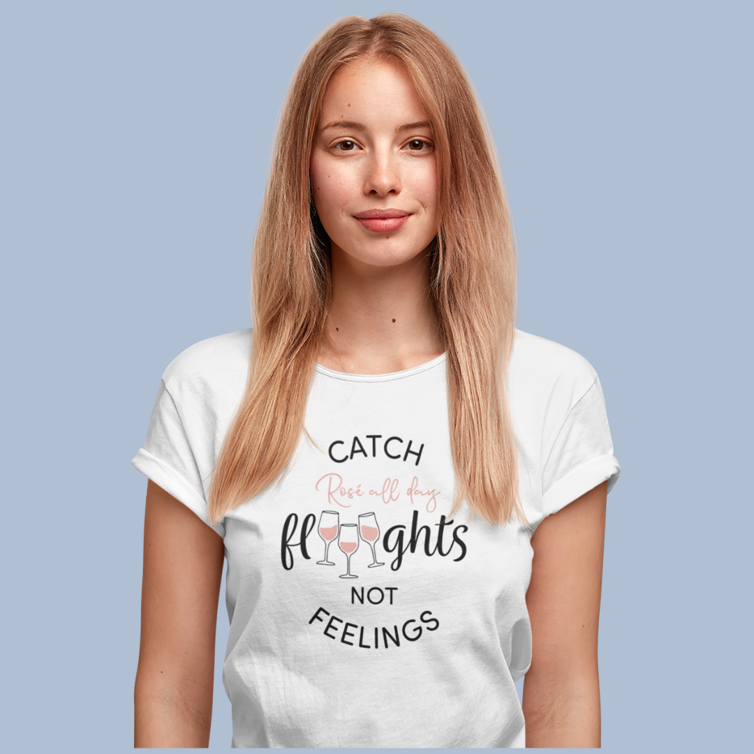 Woman wearing a white t-shirt with Catch Flights Not Feelings Rosé All Day printed on the front with wine glasses. 