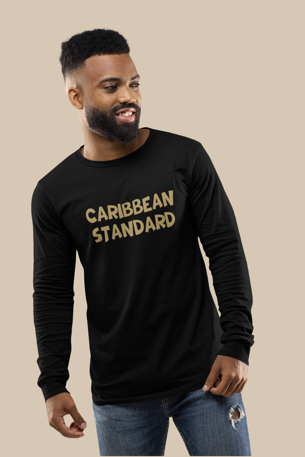 A man wearing a black long-sleeve t-shirt with 'CARIBBEAN STANDARD' printed in gold across the chest, paired with blue jeans, set against a solid beige background.