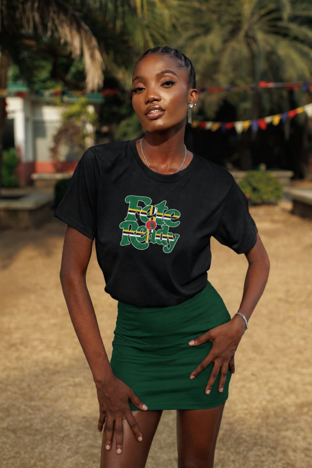 A woman wearing a black graphic t-shirt with "Fete Ready" in Dominica flag colors green, yellow, black, white and red -  paired with a green mini skirt, standing outdoors in front of a tropical background with palm trees.
Roots by GTees everyday Dominica heritage shirt, culture you wear everyday.